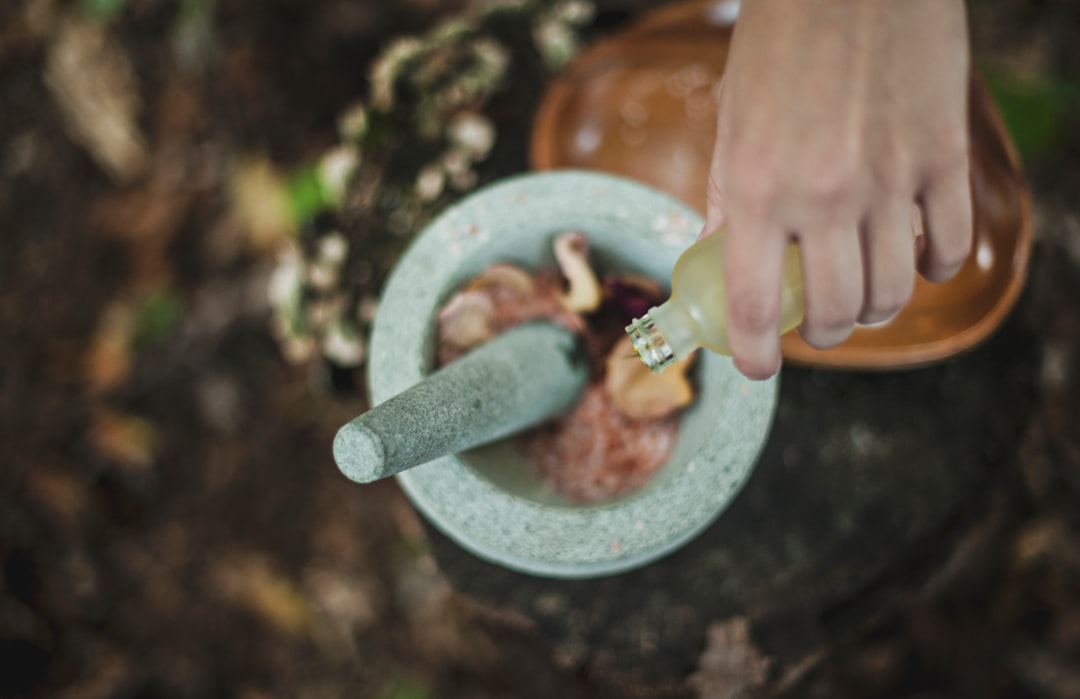 A hand pouring natural oils with a mortar and pestle, ideal for crafting hemp-infused recipes or Delta-9 drops."